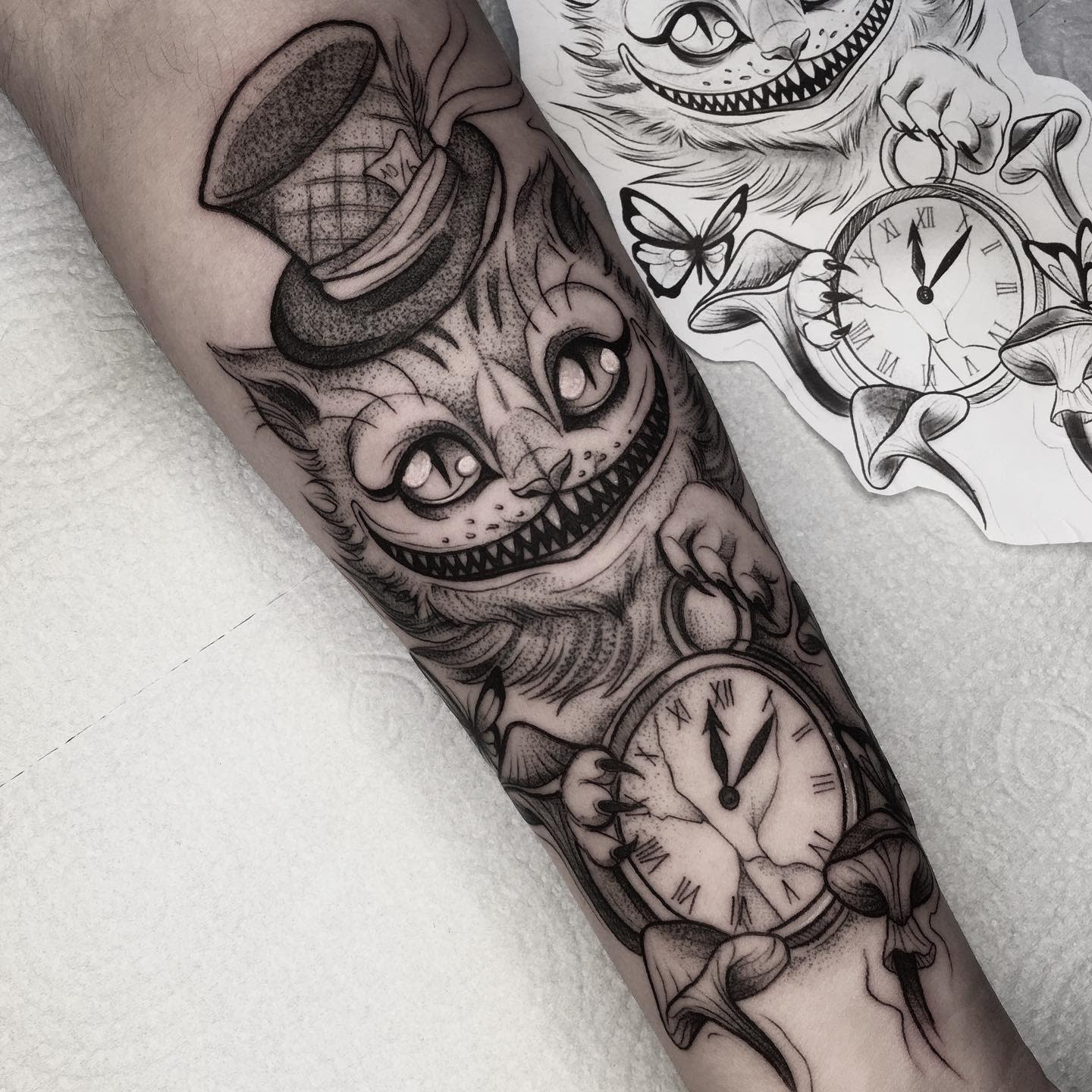 Black and grey tattoo of the Cheshire Cat with a top hat, holding a cracked pocket watch, surrounded by mushrooms